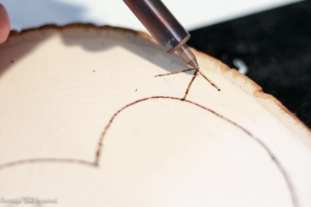 Use a wood burning tool to engrave a heart on a wood slice.