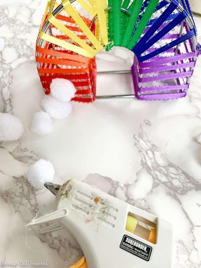 Hot glue white pom poms to the bottom of the rainbow decor to create clouds.