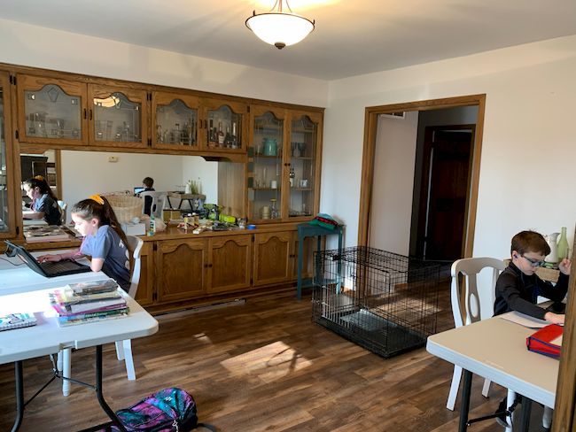 This is the BEFORE photo of a modern vintage dining room makeover. It has a dark oak built-in china cabinet and dark brown luxury vinyl plank flooring. It was set up as a temporary classroom.